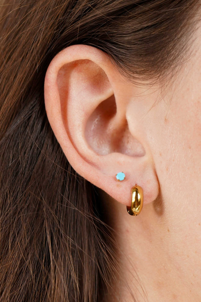 Close-up of an ear wearing a gold hoop earring and a small blue gemstone earring.