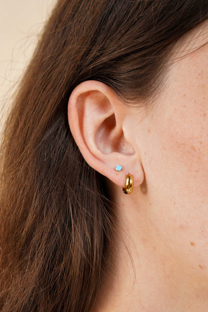 Close-up of an ear with gold hoop earrings and a blue gemstone earring.