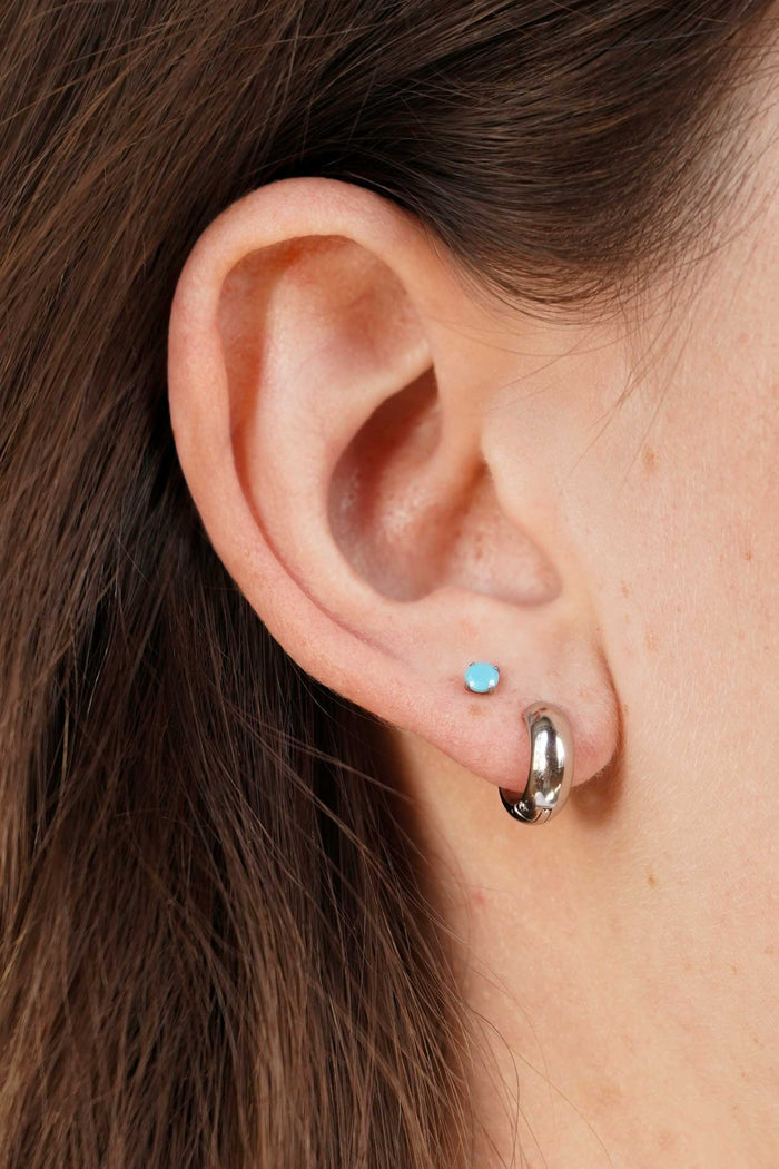 Close-up of an ear with two earrings: a small blue stud and a larger silver hoop.