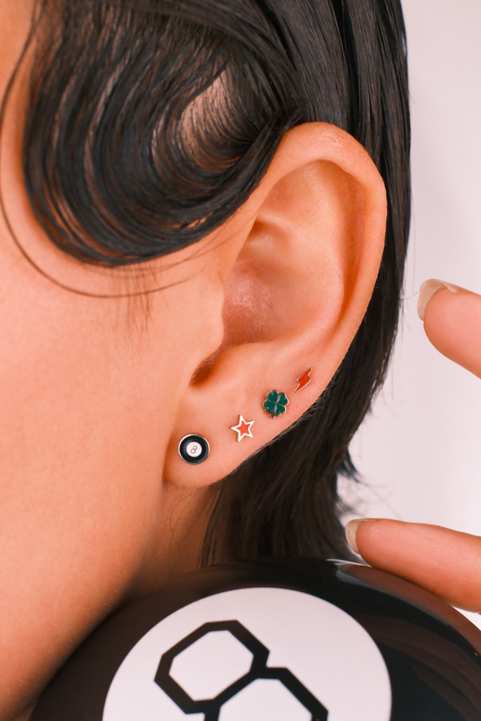 Photo of a person wearing multiple flat back stud earrings, including 1 in the shape of an 8 ball in black and white