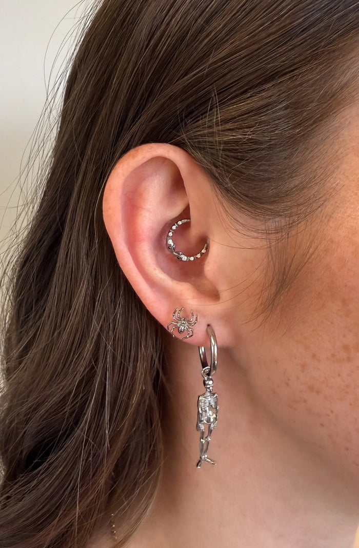 Close-up of an ear with silver hoop earrings and a dangling earring.