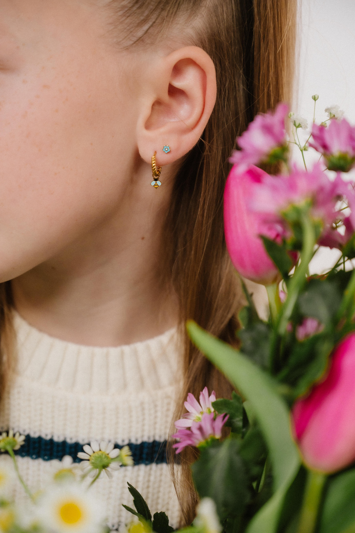 A close up of a bumblebee shaped hoop charm with yellow and black enamel and gold-plated titanium metal hanging from a hoop earring.
