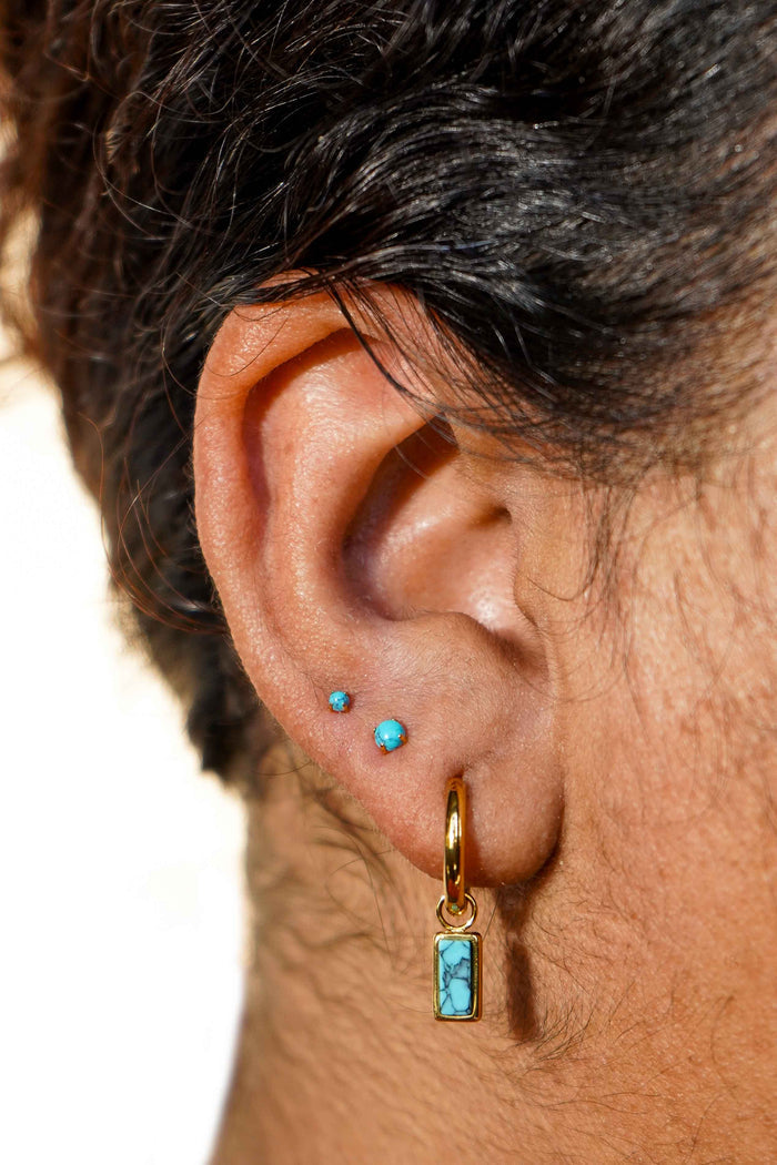 Close-up of an ear with gold hoop earrings and faux turquoise gemstones.