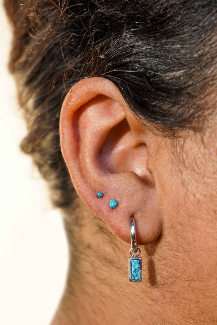 Close-up of an ear with faux turquoise stone earrings on a neutral background