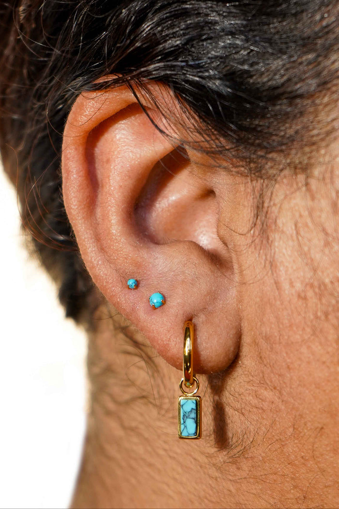 Close-up of an ear with gold hoop earrings and faux turquoise gemstones.