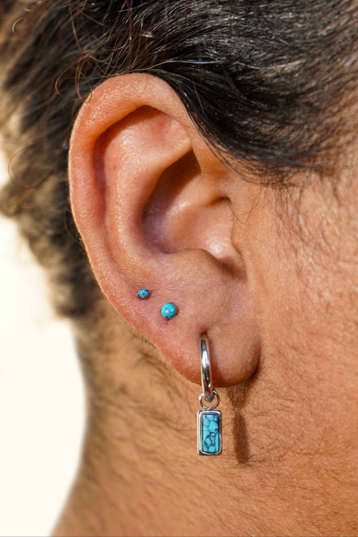 Close-up of an ear with a faux turquoise stone earring on a neutral background
