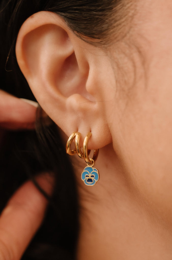 Close-up of an ear wearing gold hoop earrings with a blue enamel flower charm.