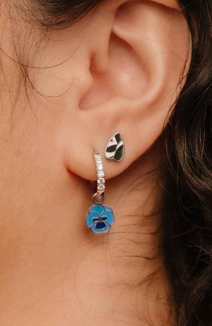 Close-up of an ear wearing silver hoop earrings with a blue enamel flower charm.