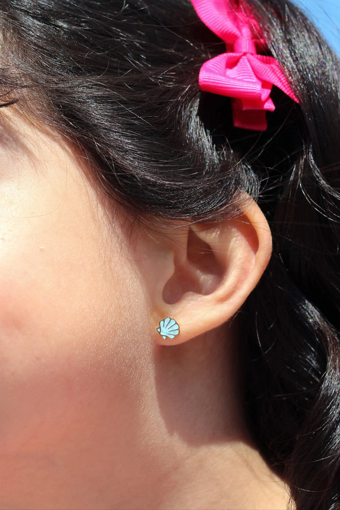 Close-up of an ear with a blue shell earring and hair with pink bows against a blue background