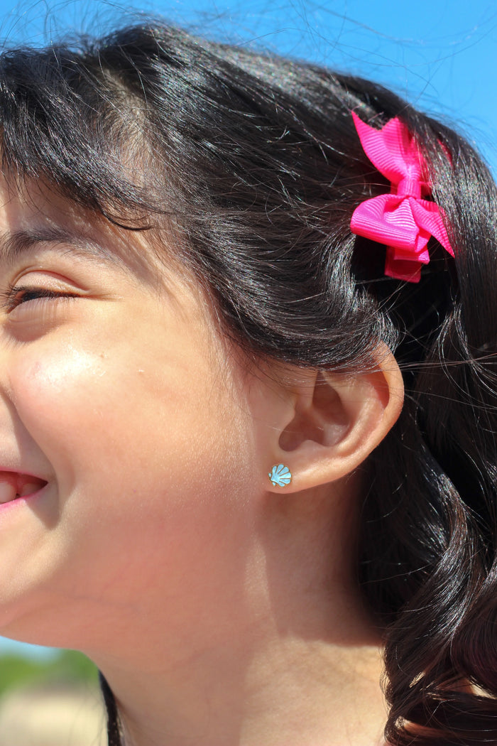Close-up of a child with a pink hair clip and blue shell earring against a blue sky.