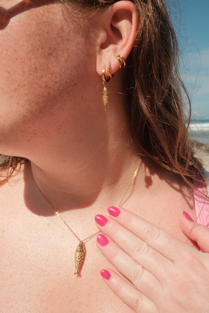 Close-up of a person wearing gold hoop earrings and a gold necklace with a beach in the background