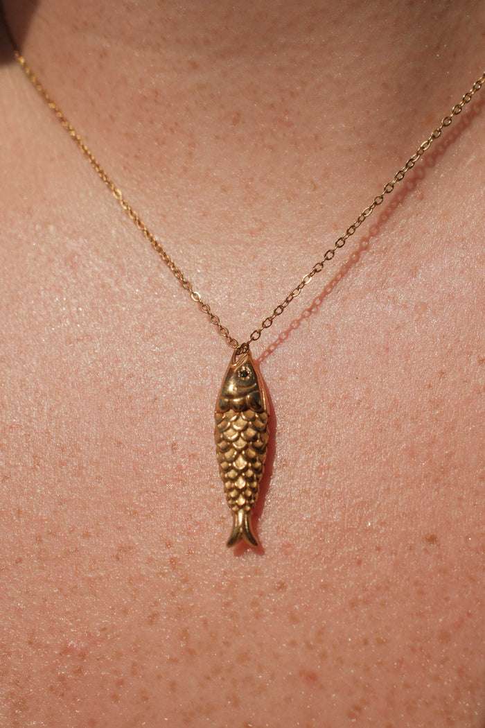 Gold fish-shaped pendant necklace on a person's neck
