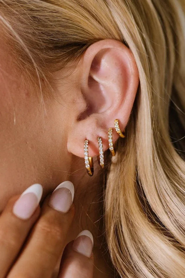 Close-up of an ear wearing gold hoop earrings with a hand adjusting them.