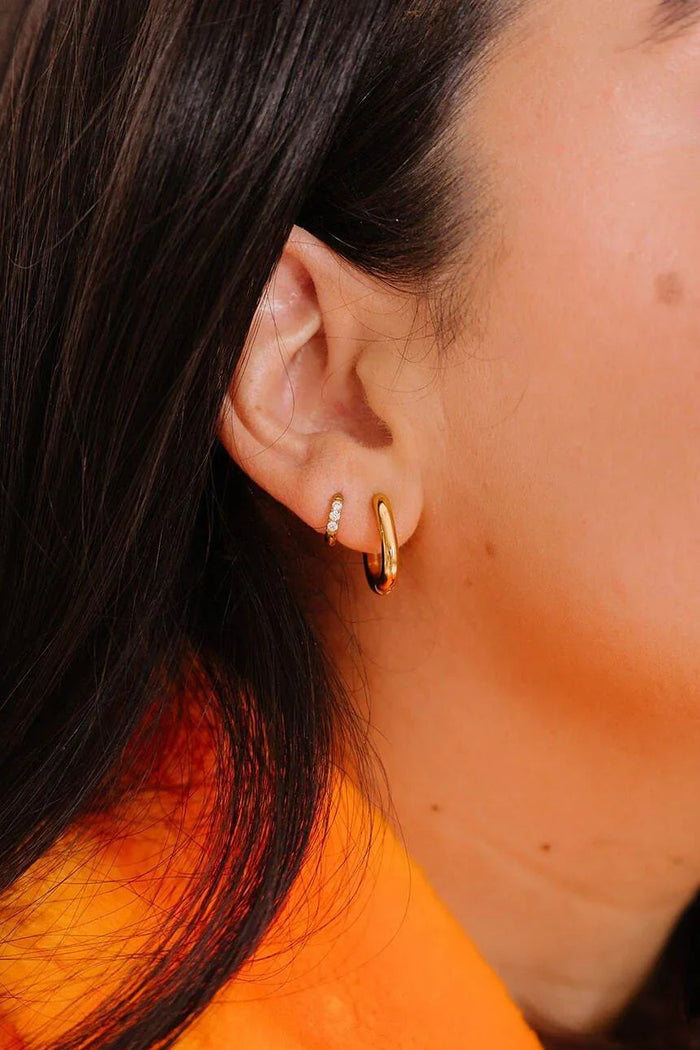 Close up of an ear with 2 styles of gold hoops on it.