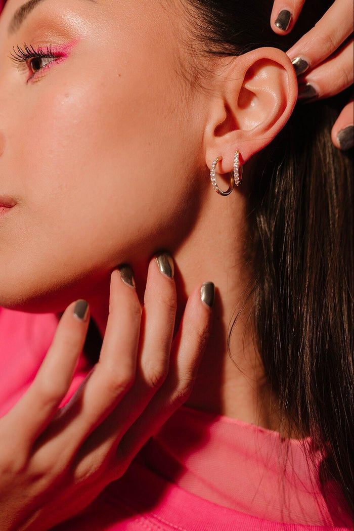Close up of an ear with 2 sizes of gold and clear CZ hoops on it.