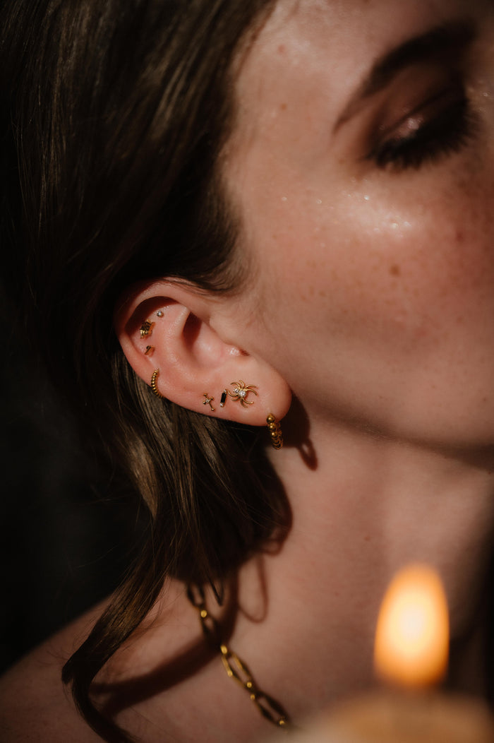 Close-up of a person wearing gold earrings with a blurred candle in the background