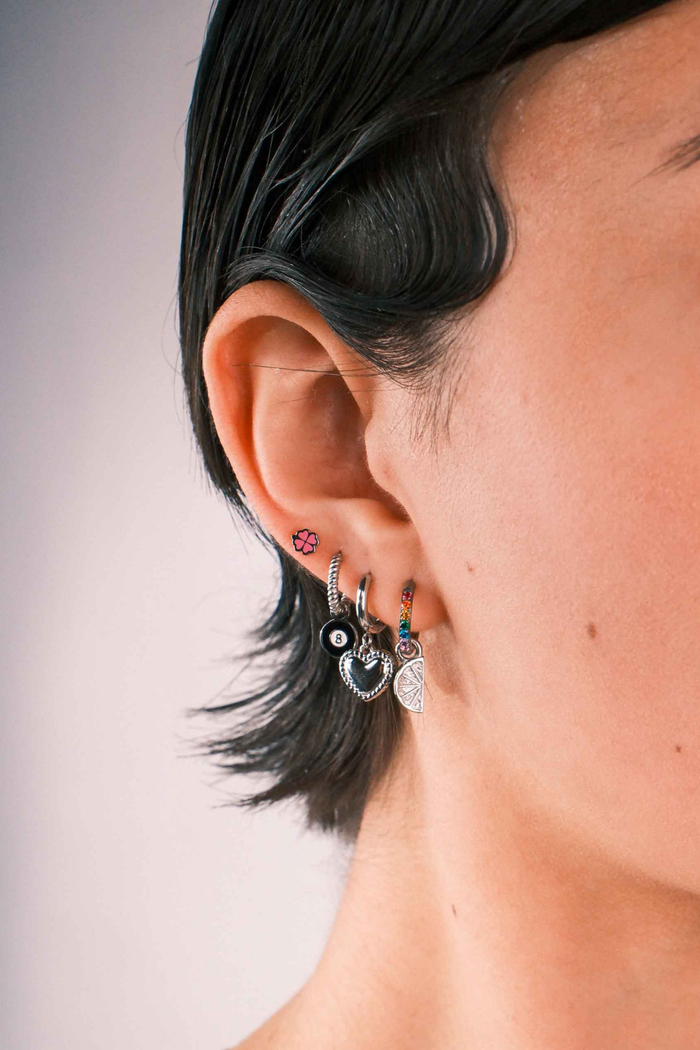 Close-up of a person wearing multiple silver earrings including a clover shaped flat back stud in pink enamel.