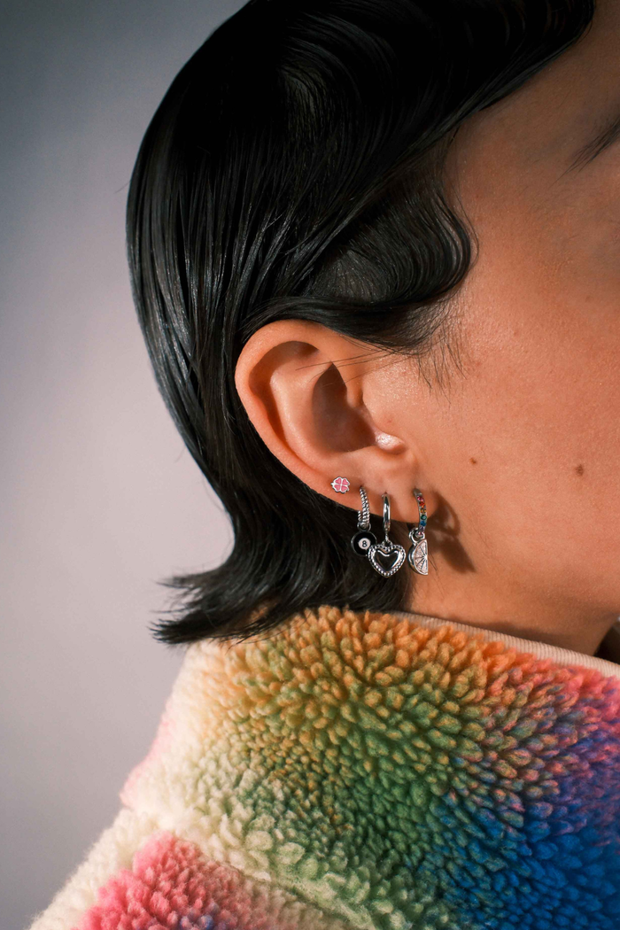 Close-up of a person wearing multiple silver earrings including a clover shaped flat back stud in pink enamel.