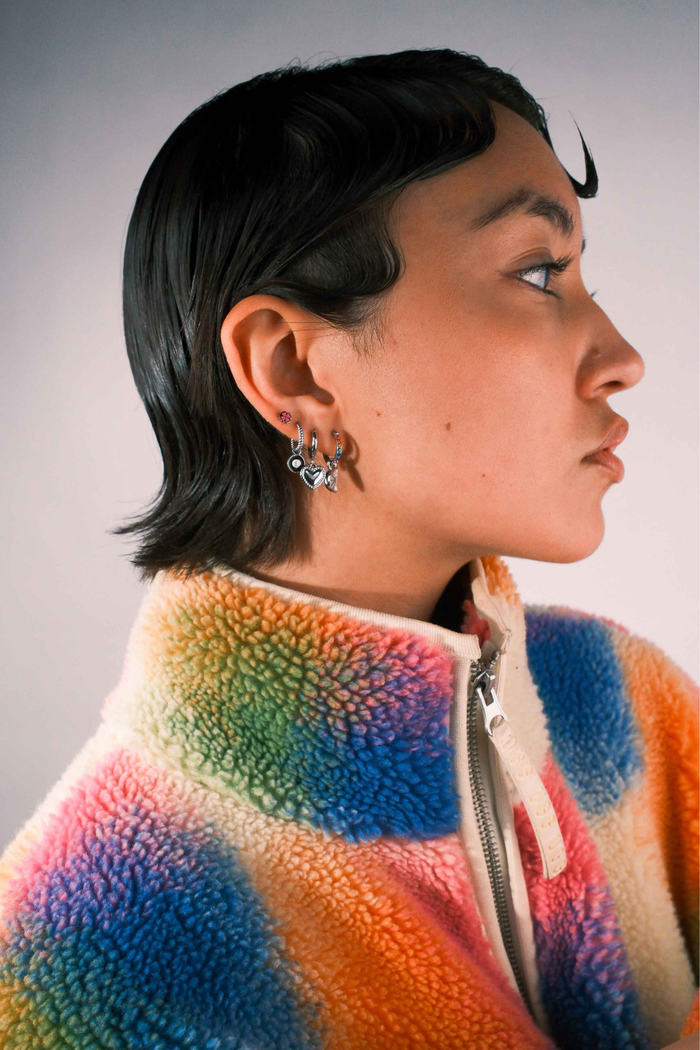 Close-up of a person wearing multiple silver earrings including a clover shaped flat back stud in pink enamel.