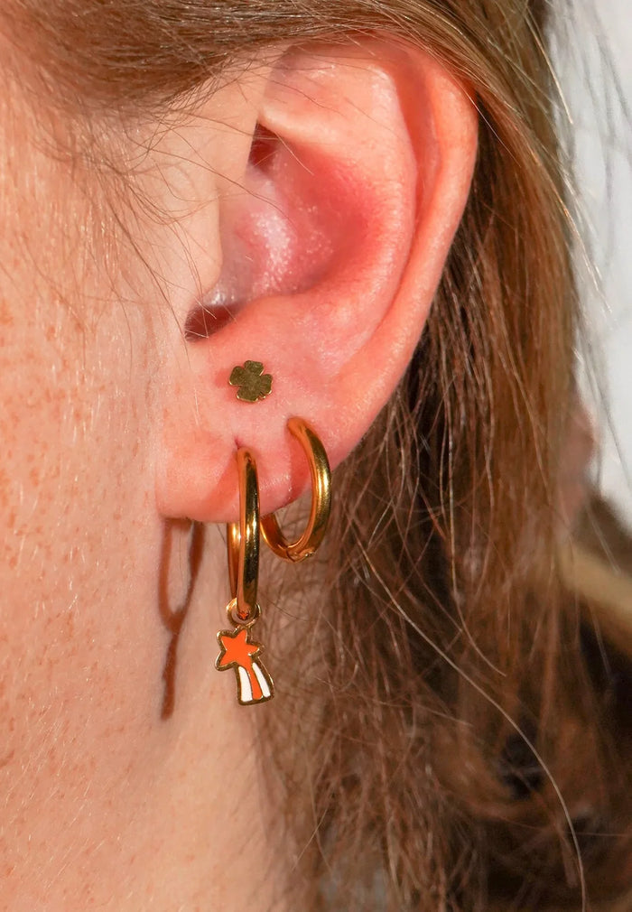 Close-up of an ear wearing gold hoop earrings with star and clover charms.