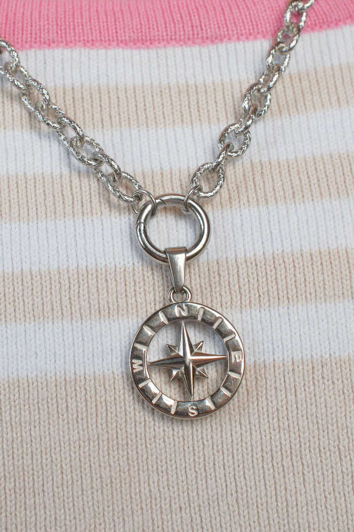 A silver compass pendant necklace resting on a pink and cream striped knit sweater.