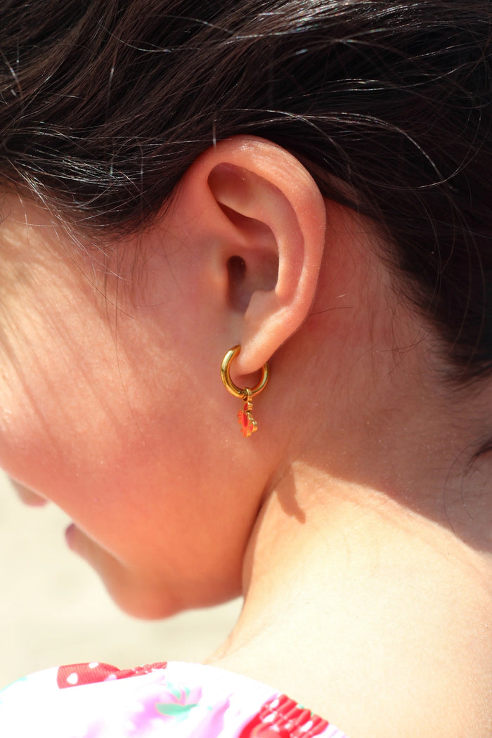 Close-up of an ear wearing a gold hoop earring with red crab charm on it.