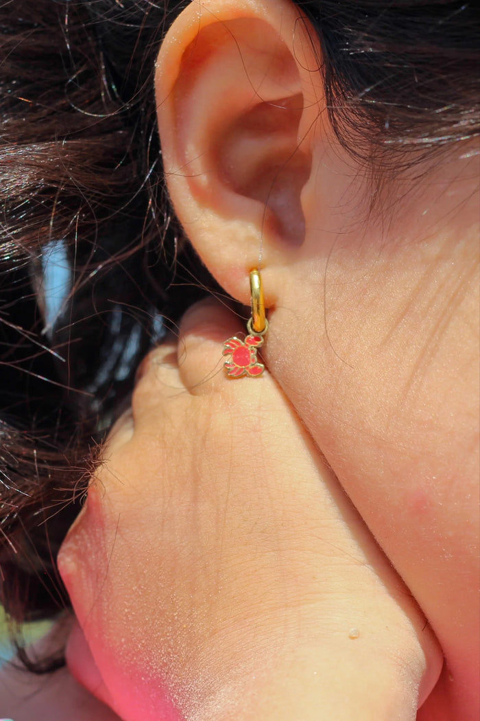 Close-up of an ear wearing a gold hoop earring with red crab charm on it.
