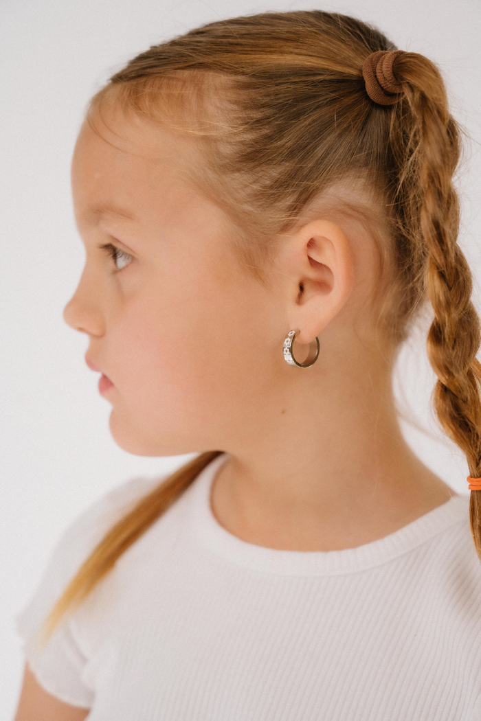 Profile of a girl with silver hoop earrings braided hair wearing a white shirt on a plain background
