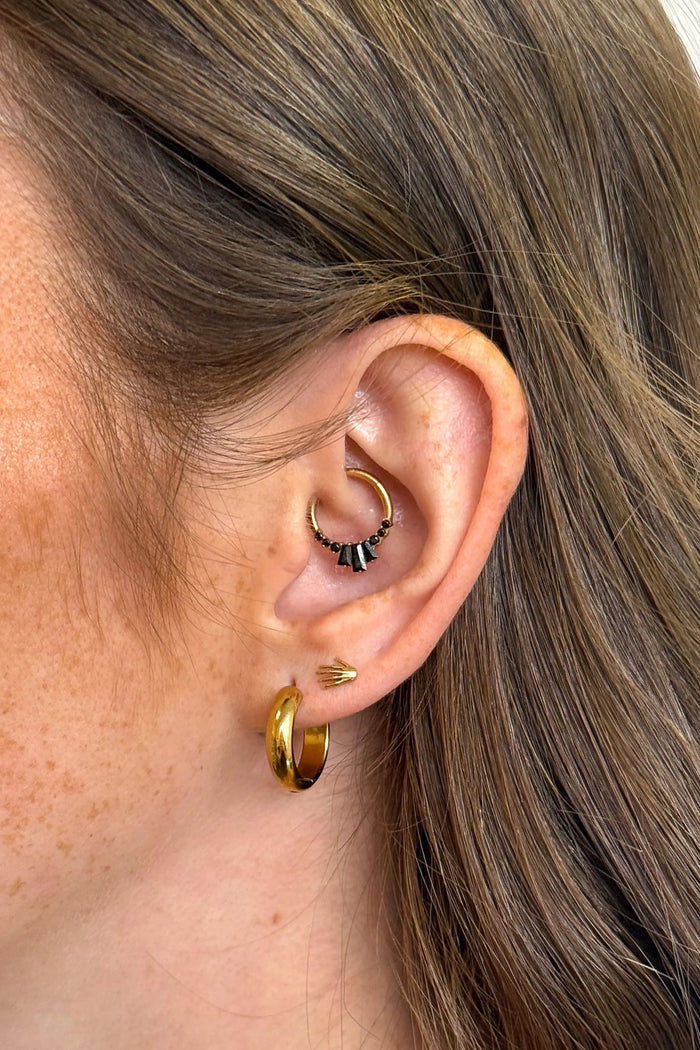 Close-up of an ear with gold hoop earrings and a small black and gold earring.