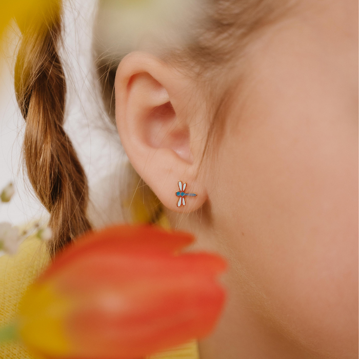 A close up of a dragonfly shaped flat back stud earring with blue enamel and gold-plated titanium metal.