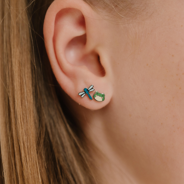 A close up of a dragonfly shaped flat back stud earring with blue enamel and titanium metal.