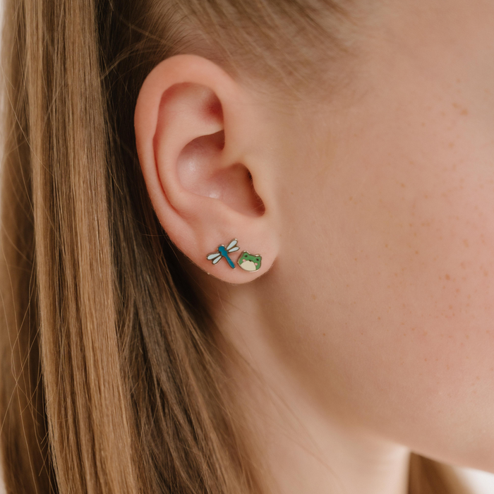 A close up of a dragonfly shaped flat back stud earring with blue enamel and titanium metal.