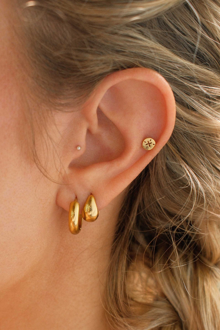 Close-up of a person wearing gold earrings with a blurred background