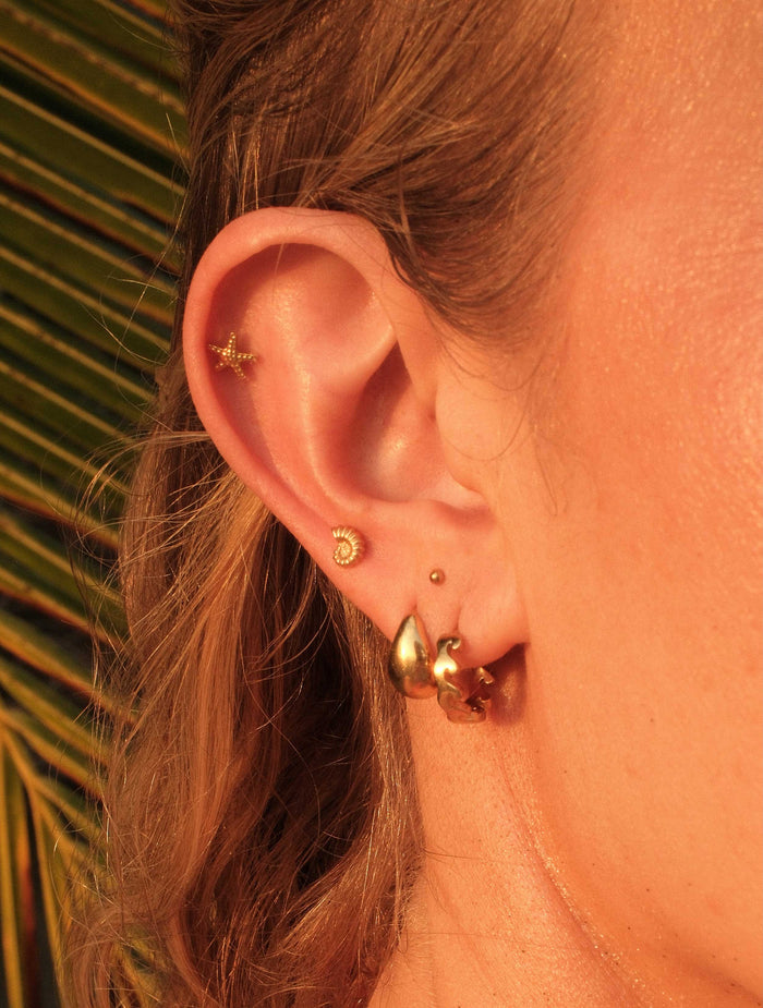 Close-up of an ear with gold earrings against a blurred natural background