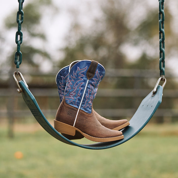 Pair of kids' Durango Shyloh cowboy boots on a playground swing with a blurred outdoor background