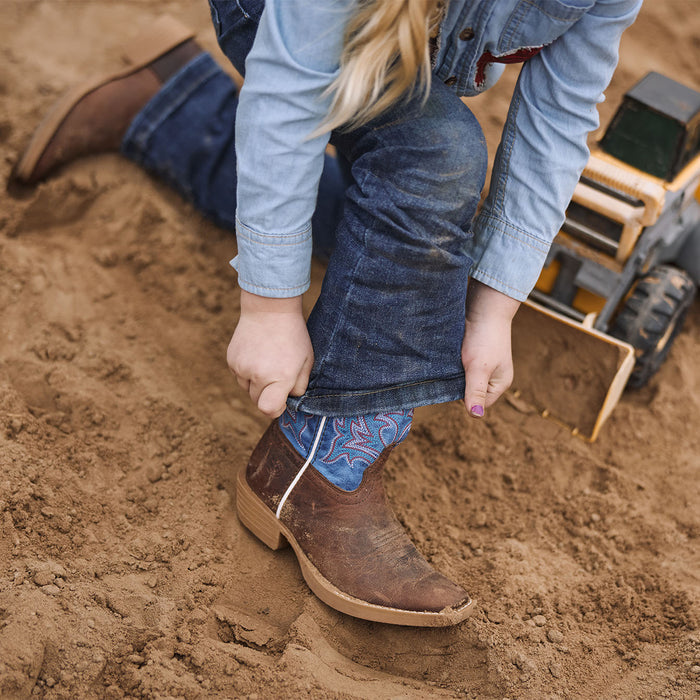 Kid wearing brown and blue cowboy boots in a sandy play area.