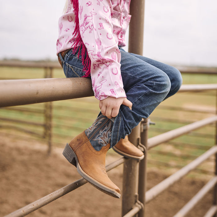 Kid wearing Durango Shyloh Kids cowboy boots sitting on a fence in an arena.
