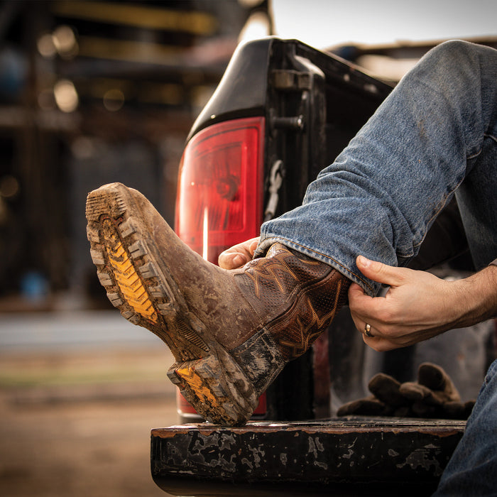 Person adjusting a work boot on a vehicle's tail light with a blurred background
