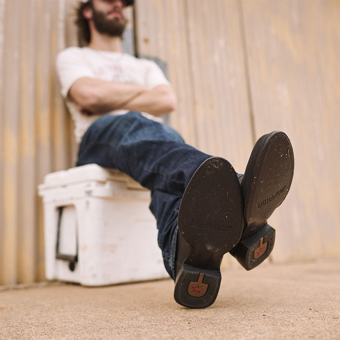 Person sitting in a cooler with feet up wearing black Durango roper boots with leather sole.