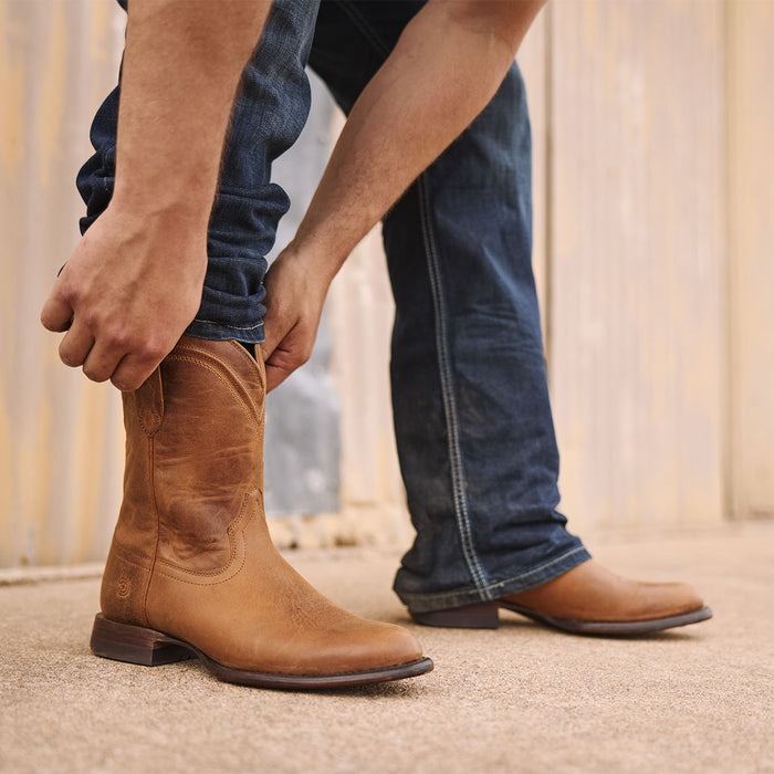 Man wearing Durango Roper boots adjusting the pull straps with blue jeans.