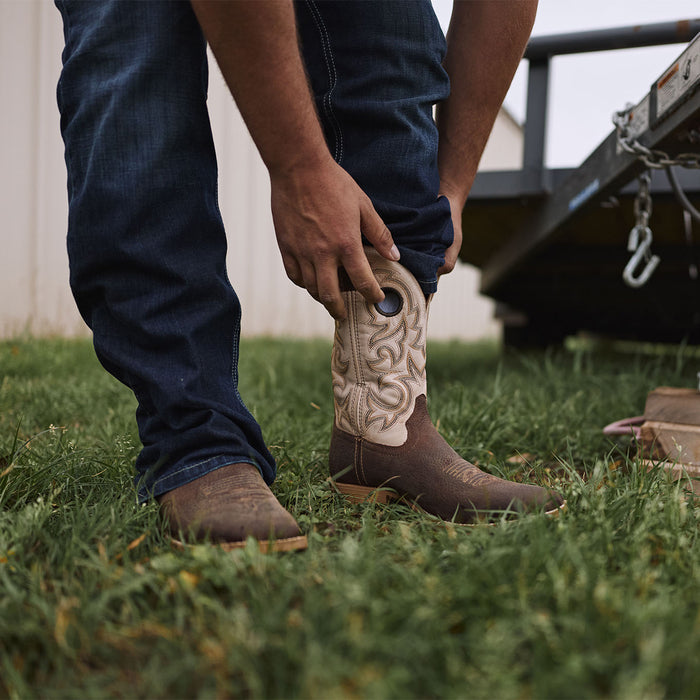 Man adjusting pants over Durango Shyloh cowboy boots near a trailer on grass.