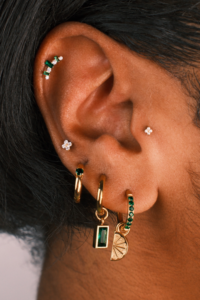 Close-up of an ear with multiple earrings including gold, green, and silver pieces.
