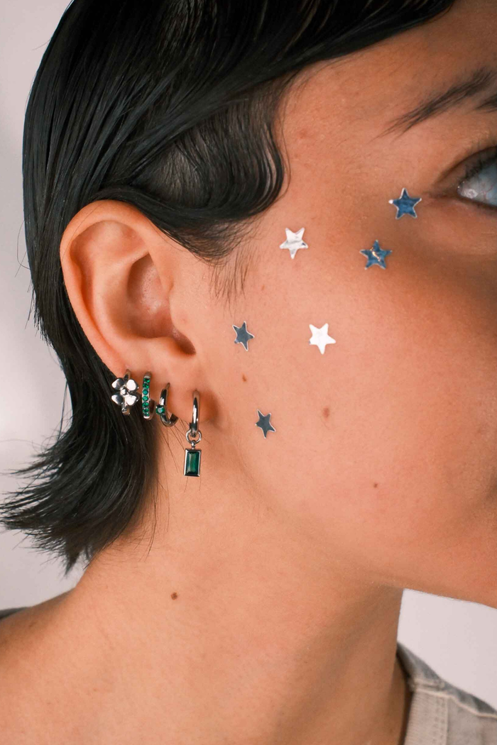 Close-up of a person wearing multiple earrings including a hoop with a channel of emerald green zirconia stones