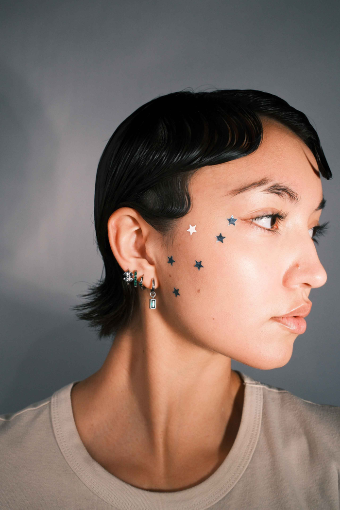 Close-up of a person wearing multiple earrings including a hoop with a channel of emerald green zirconia stones