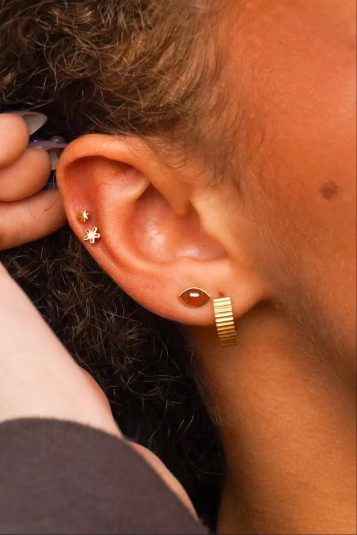 Close-up of an ear with gold hoop earrings and a small stud, with a hand adjusting something near the ear.