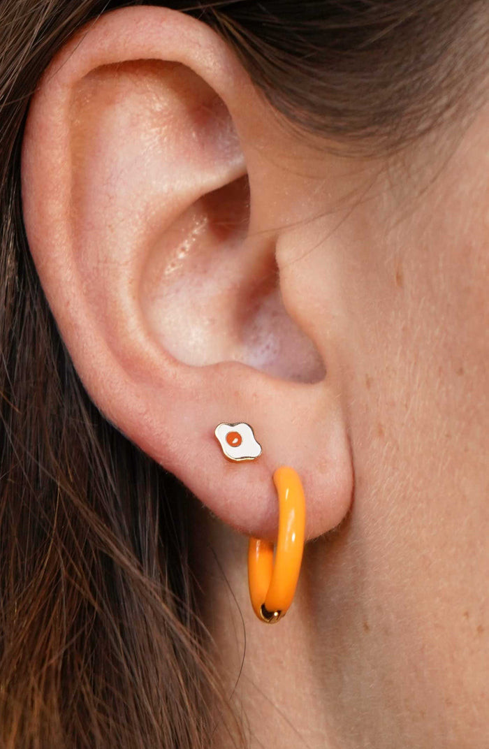 Close-up of an ear with a small earring and a larger orange hoop earring.