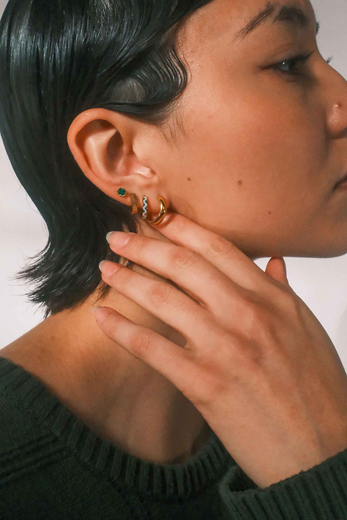 Close-up of a person wearing multiple gold earrings with a neutral background