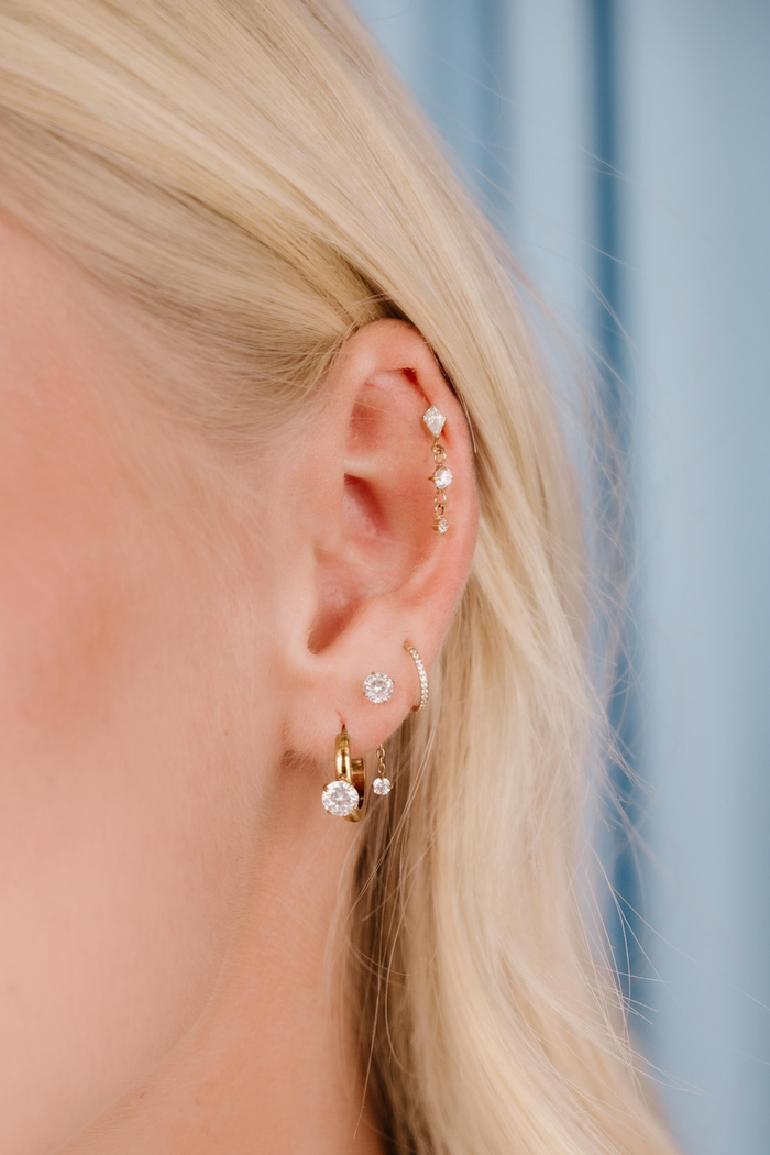 Close-up of a person wearing multiple gold earrings with clear gemstones against a blurred background.