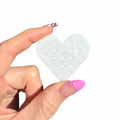 Heart-shaped acrylic piece with tiny evenly-placed holes, held by a hand with pink nail polish on a white background