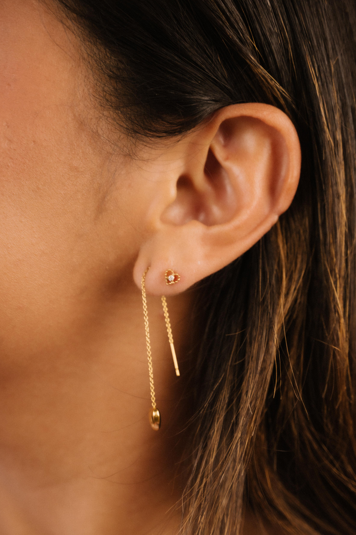 Close-up of an ear wearing a gold earring with a dark background